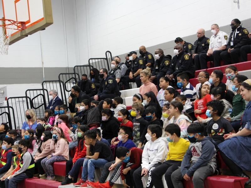 students and public safety workers sit in the bleachers at a school assembly