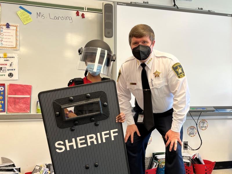 Sheriff with student trying on protective shield and helmet
