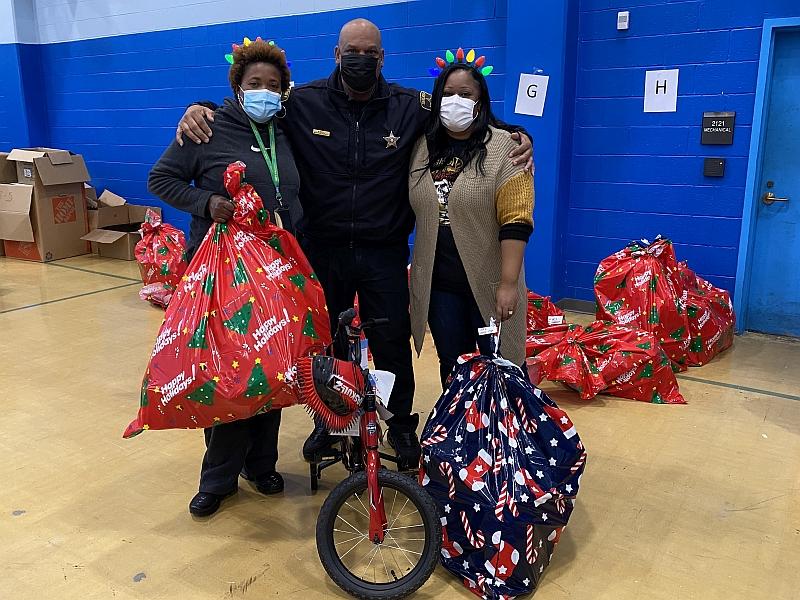 deputy and two civilians with child's bicycle and large holiday gift bags