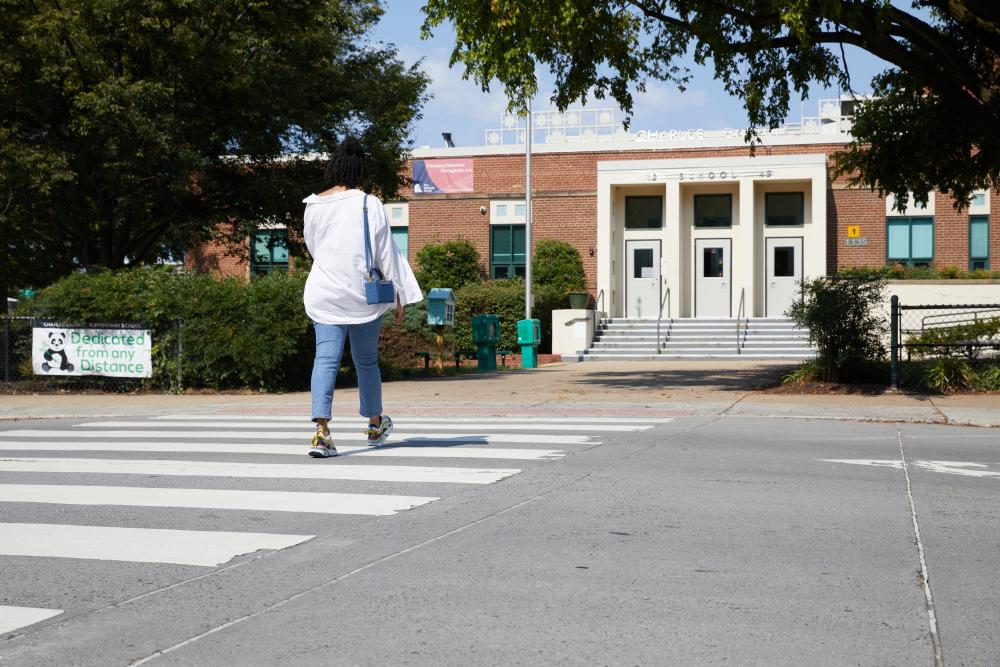 An individual walking across a crosswalk to Charles Barrett Elementary School