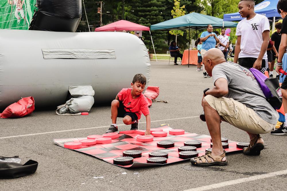 A little boy in red and a man in gray are playing lawn-size red and black checkers