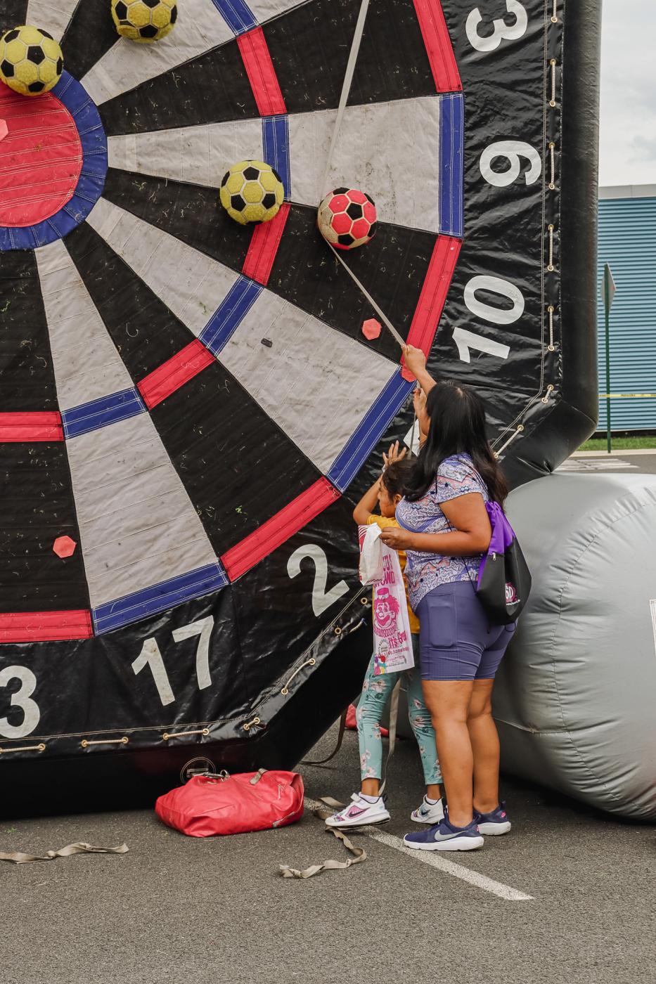 Mom helping her daughter get the soccer ball down from a big blow-up soccer dart