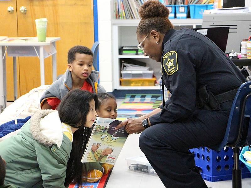 deputy showing a book to three young children