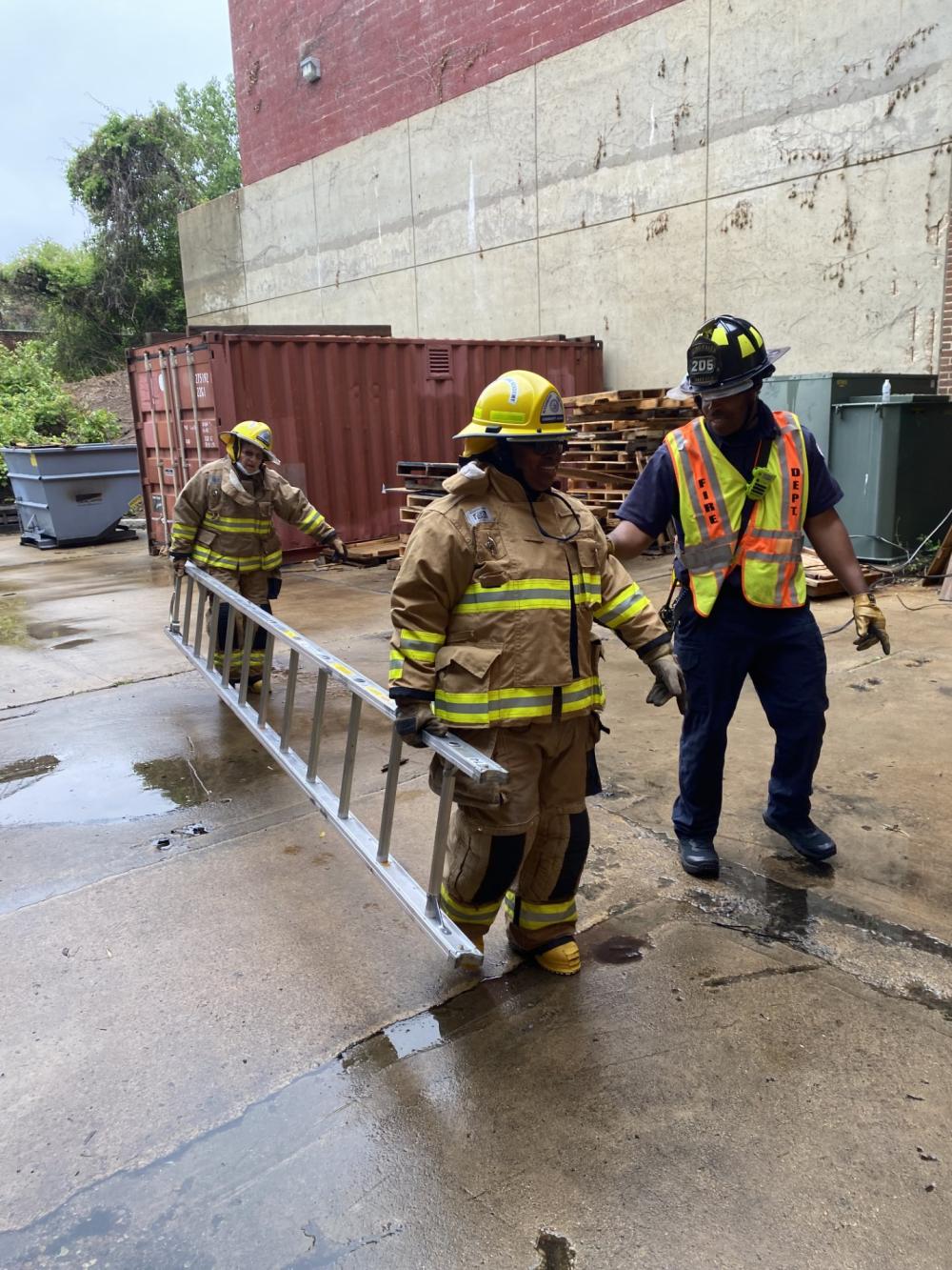 Community Fire Academy participants carry a ladder with the guidance of a first responder during a hands-on session at AFD's training facility.