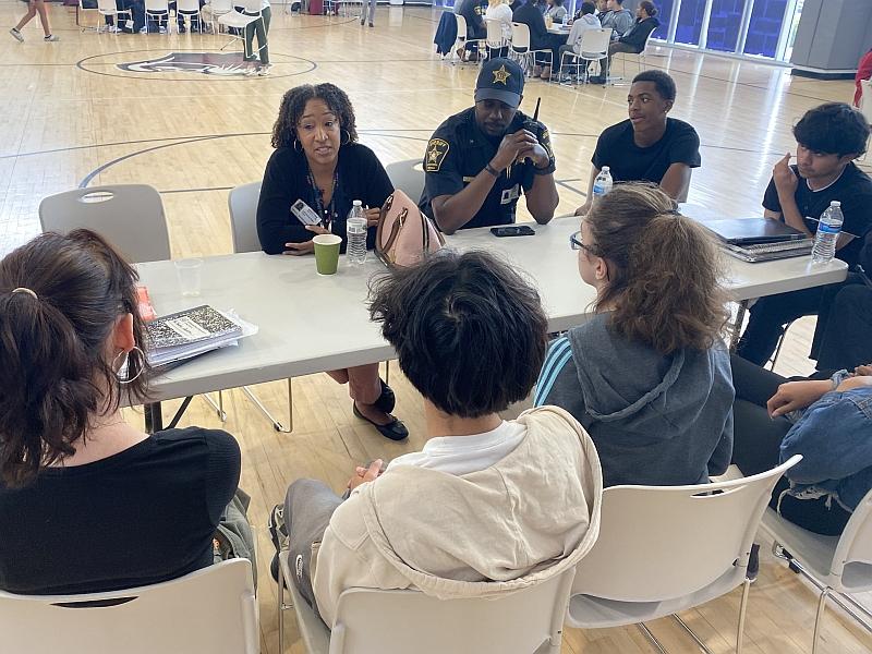 civilian employee and deputy seated and talking with small group of middle schoolers