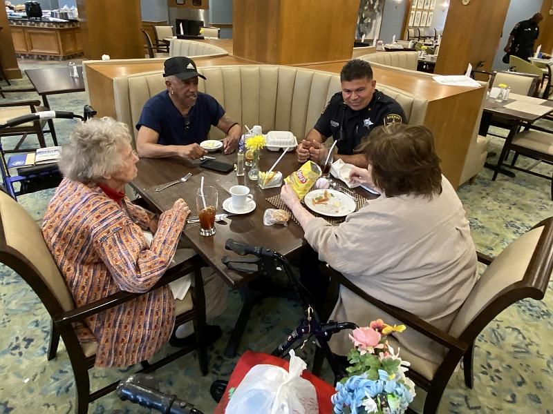 deputy sitting at small dining table with three senior citizens enjoying lunch