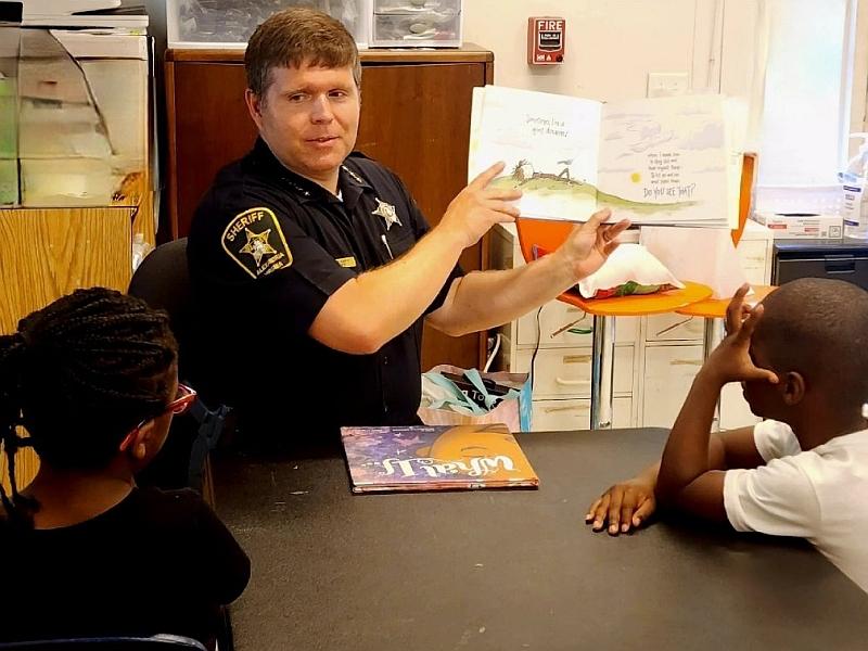 sheriff holding a children's book open and reading to two children at a table
