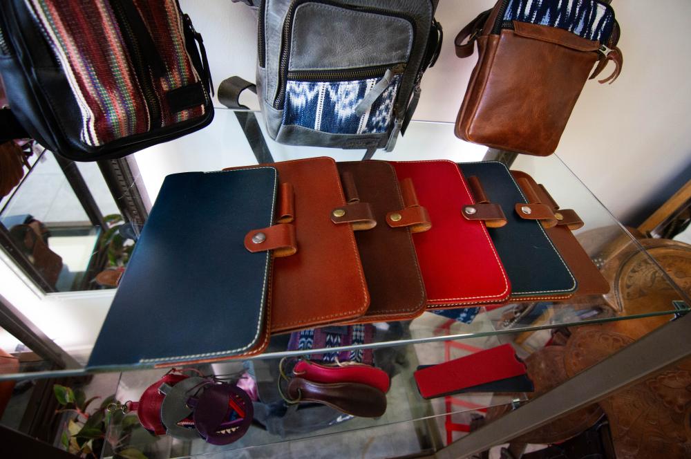A row of leather folios lie on top of a glass display case. The folios are blue, brown and red.