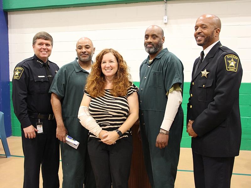 Sheriff in uniformed, member of City Council, deputy in uniform and two inmates wearing green jumpsuits standing together