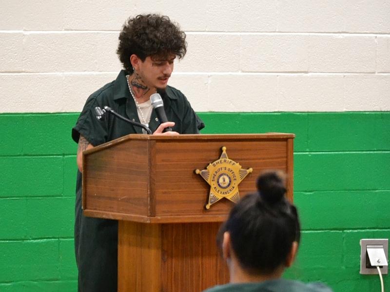 inmate in jumpsuit speaking at podium