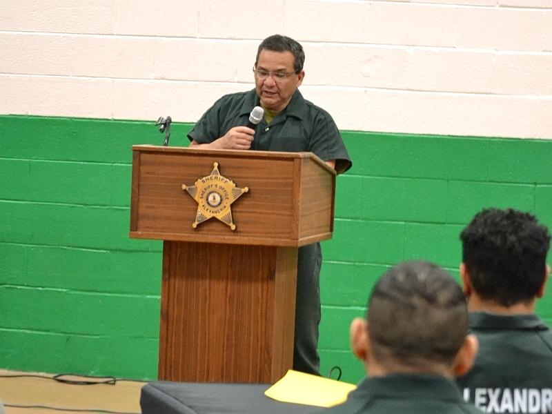 inmate in jumpsuit speaking at podium