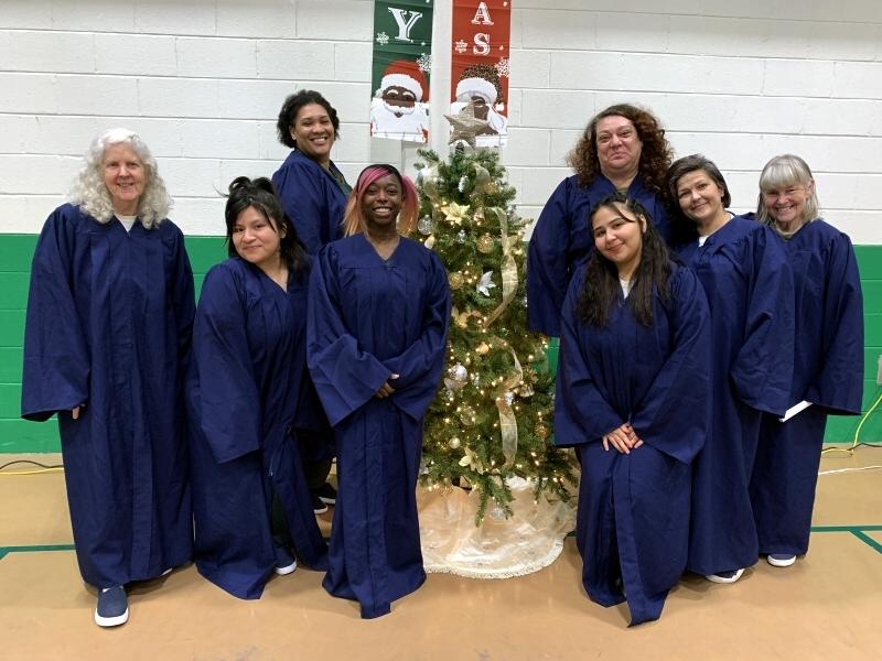 eight women in blue choir gowns standing around a Christmas tree