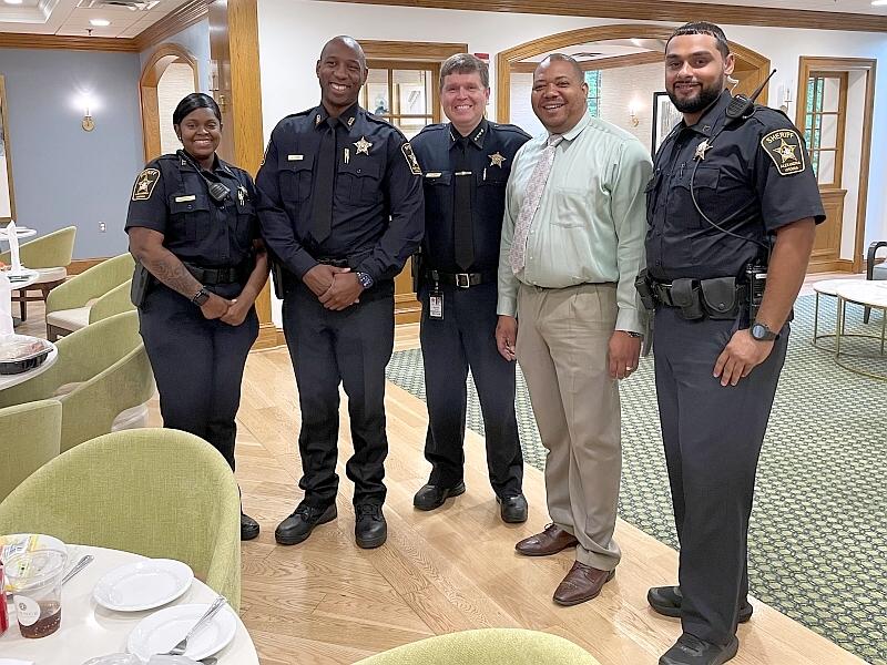 Sheriff and three deputie standing with business person inside the dining room of a senior living facility