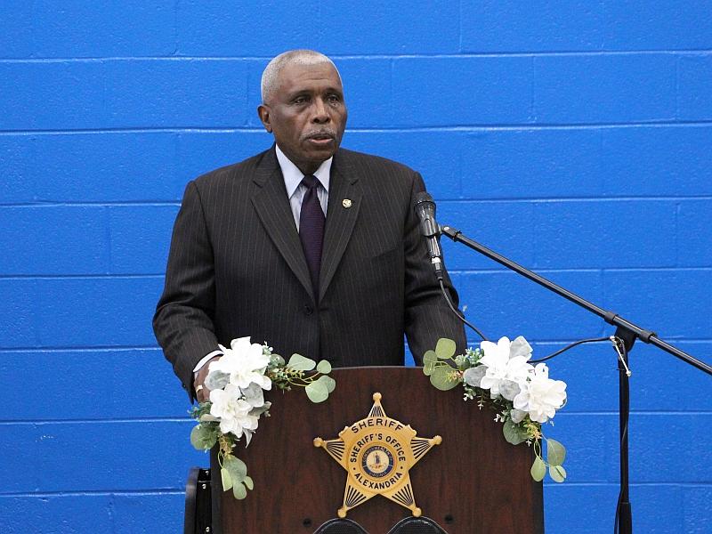 Man in suit speaking at podium with Sheriff's star in front