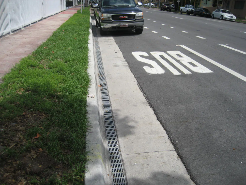 A photo of narrow grate running along the curbside of a roadway.