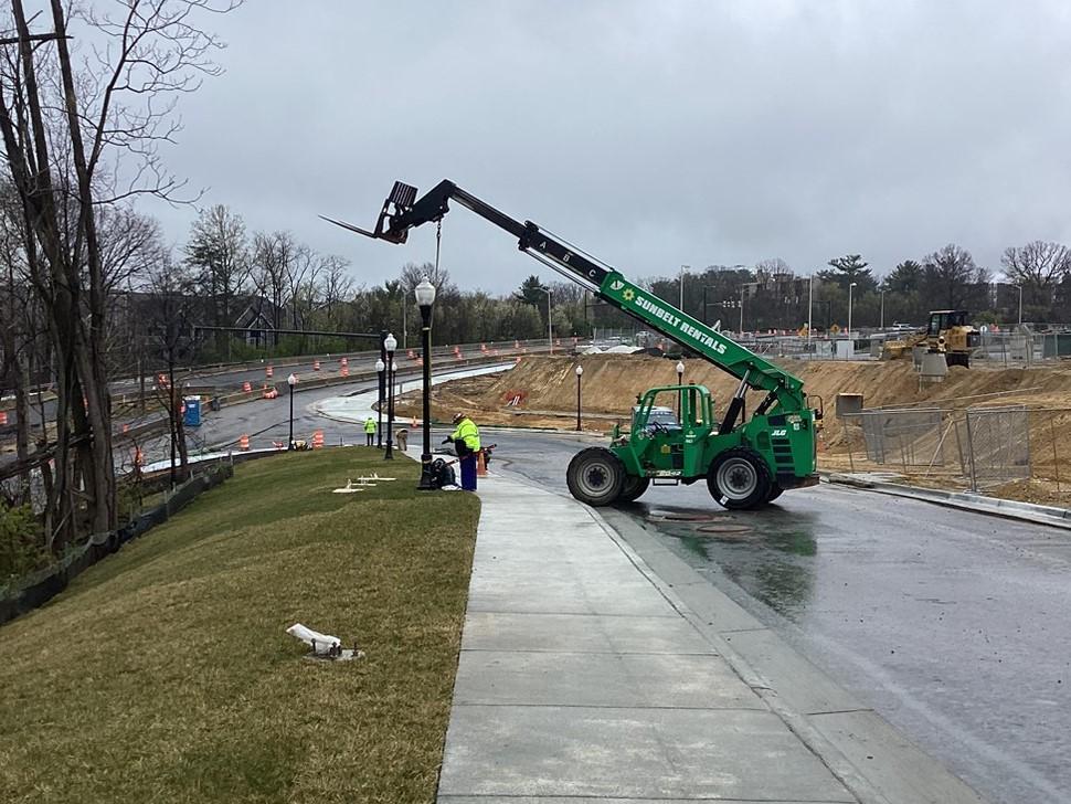 Photo of light pole being lowered into place next to a sidewalk along Road 7 on March 27, 2024