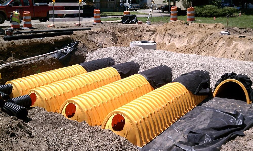 A photo of a several large plastic storage chambers that have been installed in an open excavation in the middle of a parking lot.