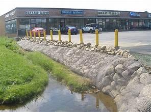 Photo of a water channel with banks that are protected with a layer of large rocks. The rocks are held in place with thick wire baskets that are anchored in place.