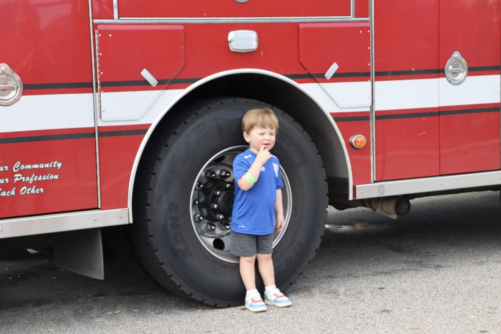 Little child wearing a blue shirt standing by the fire truck's back wheel