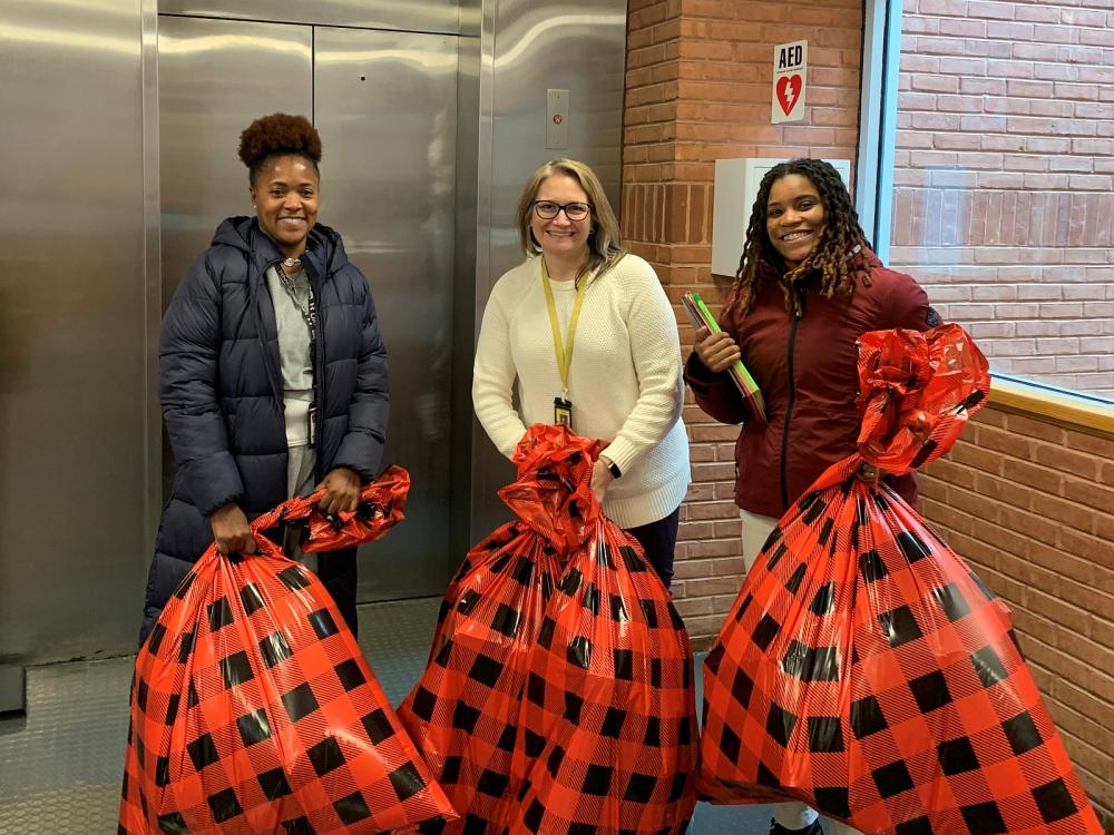 three professional staff members smiling and each holding an oversized plastic gift bag with a red and black design