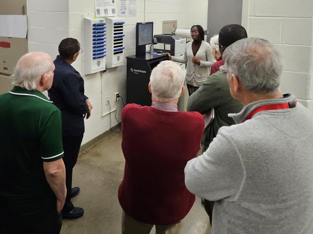 Deputy in civilian clothing explaining the livescan computer for fingerprinting to a group of community members in the jail