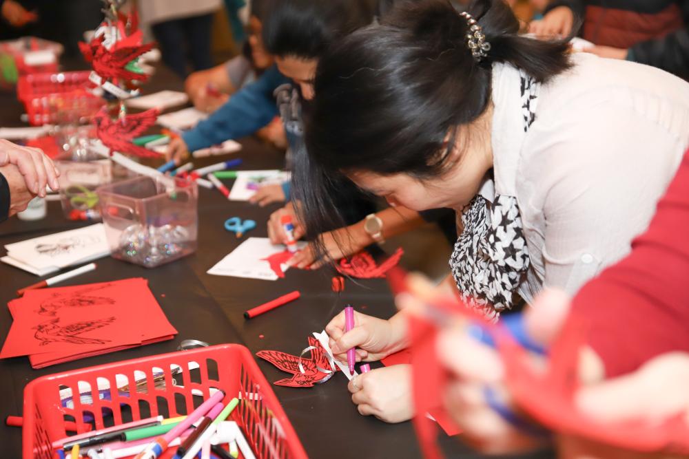 A group of people at a table participate in a craft with paper, scissors, and colored markers. 