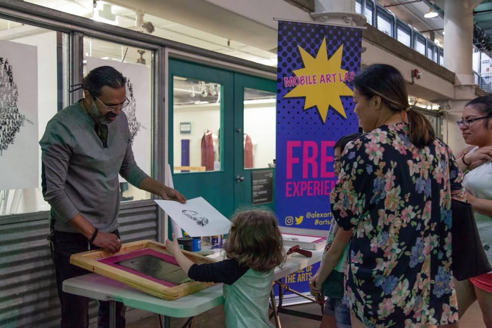 A woman and a child work on a screen-printed art piece. 