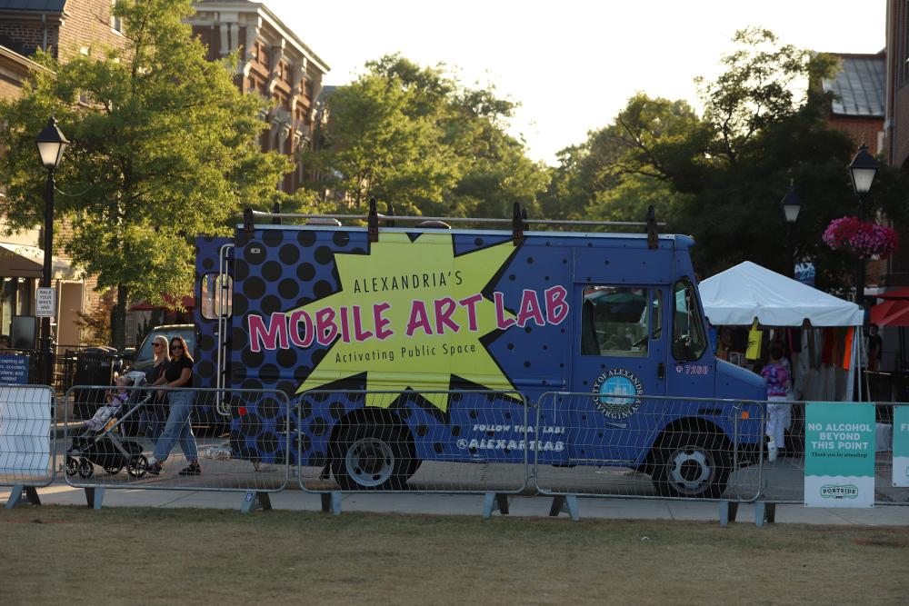 A purple van with the words "Mobile Art Lab" is parked during a community event. 