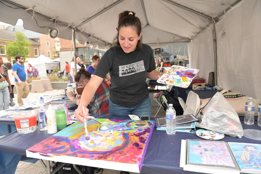 A woman paints a colorful abstract canvas at an outdoor event.