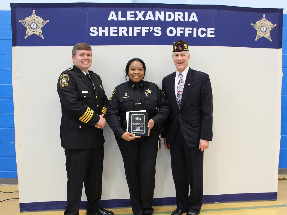Sheriff in formal uniform, deputy in blue uniform holding award plaque and official in civilan attire wearing American Legion hat 