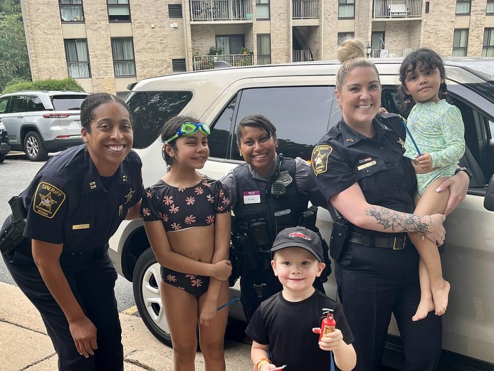 Sheriff's commander in blue uniform, Sheriff's sergeant in blue uniform and Police officer in gray uniform with three kids, all smiling
