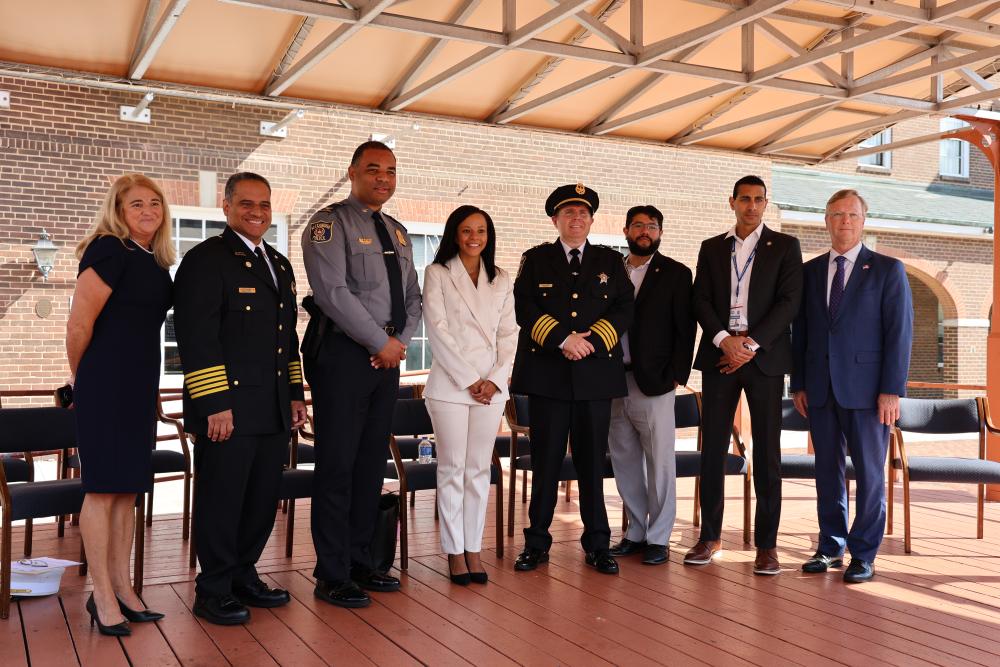 Group of eight diverse professionals in formal and uniform attire, including fire, sheriff, and police officials, standing together at an outdoor event. 