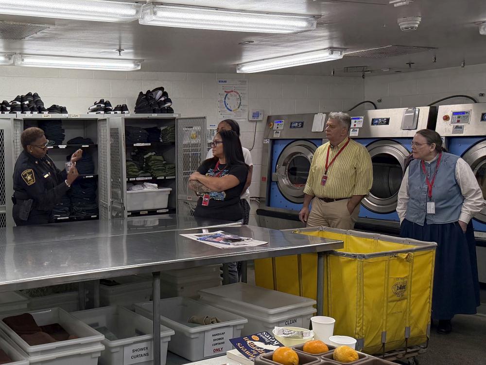 In a jail laundry room, deputy speaks with four community members on a tour