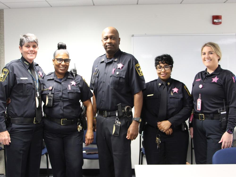 Five deputies wearing pink badges on their blue uniforms in support of Breast Cancer Awareness Month
