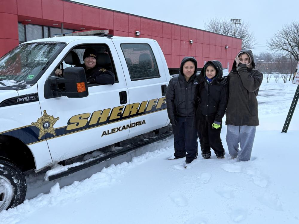 Sheriff in plow truck with three community members nearby in a snowy parking lot