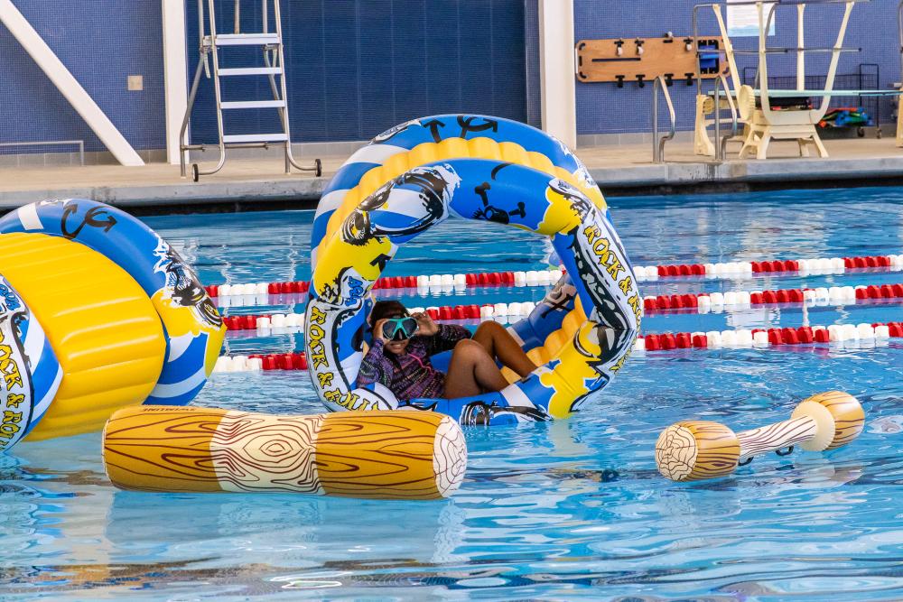 Pool toys and blow ups on the water, while a child is inside one of the blow up wheel