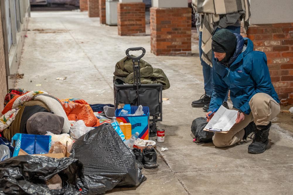 person kneeling to talk to person sleeping outside in a portico