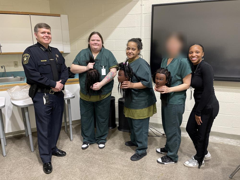 Sheriff and braiding instructor standing with three students in the middle who are holding mannequin heads with braided hair