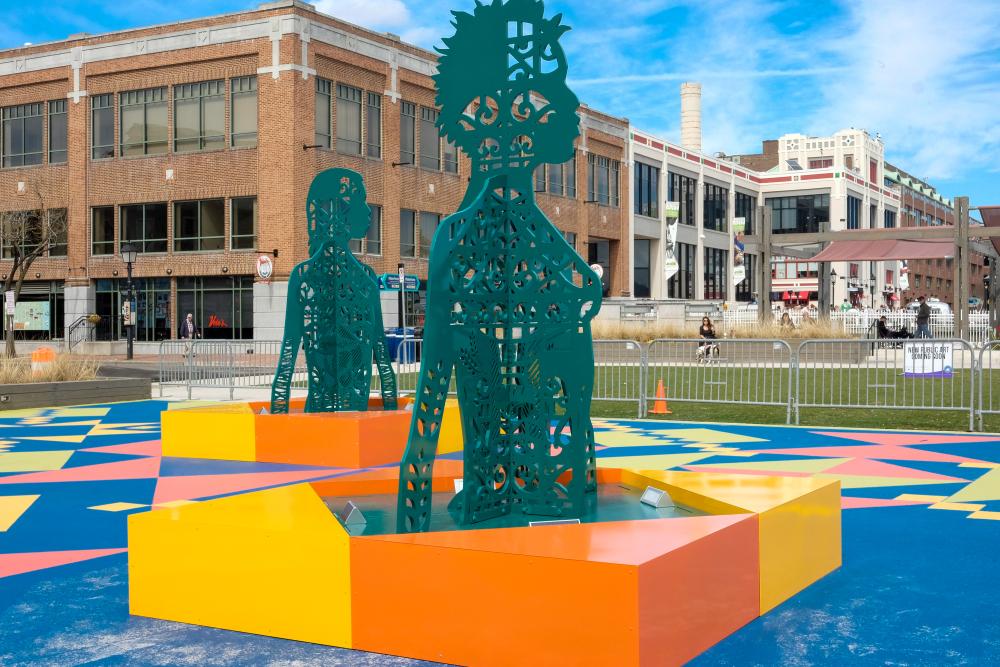 Site See Installation with human figures from torso up in green metal with holes and an orange and yellow square foundation