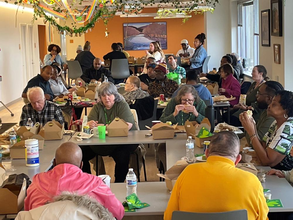 Photo of people eating a casual lunch together in a large room at multiple tables