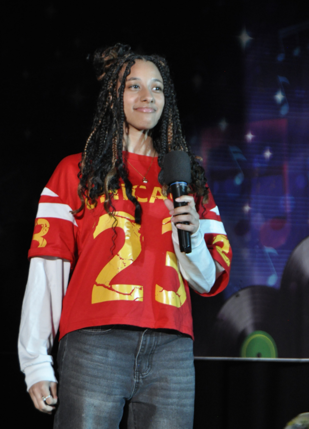 Teen girl dressed in football jersey and white long sleeve undershirt holding a mike