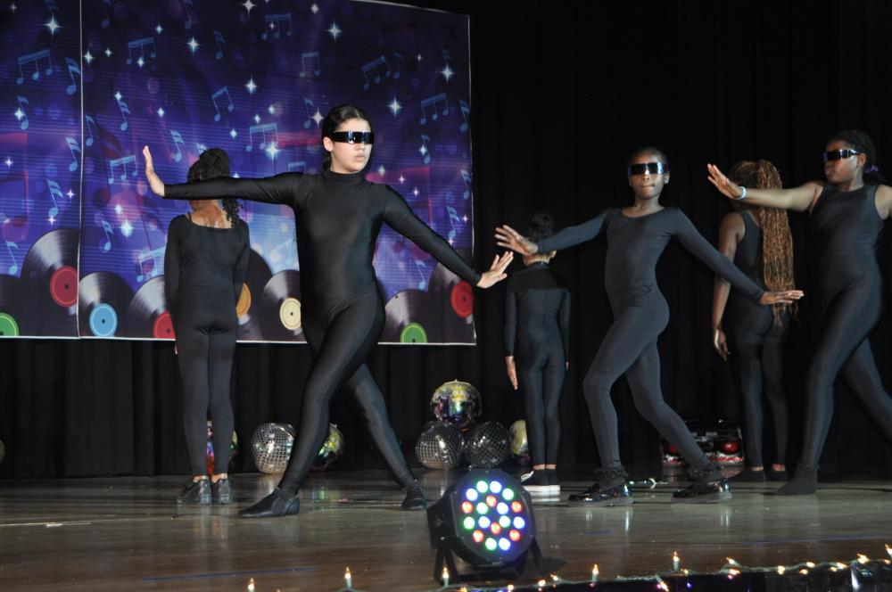 Group of girls in all black with black covers on their eyes dancing on stage