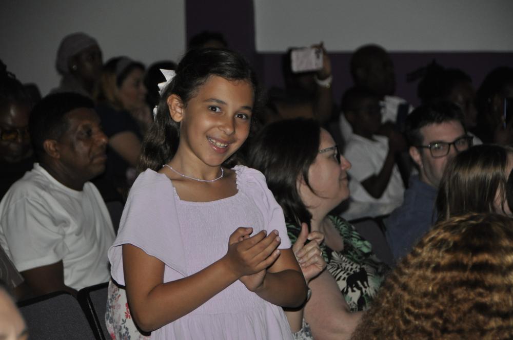 Girl with a white bow and lavender dress smiling for the camera among the crowd