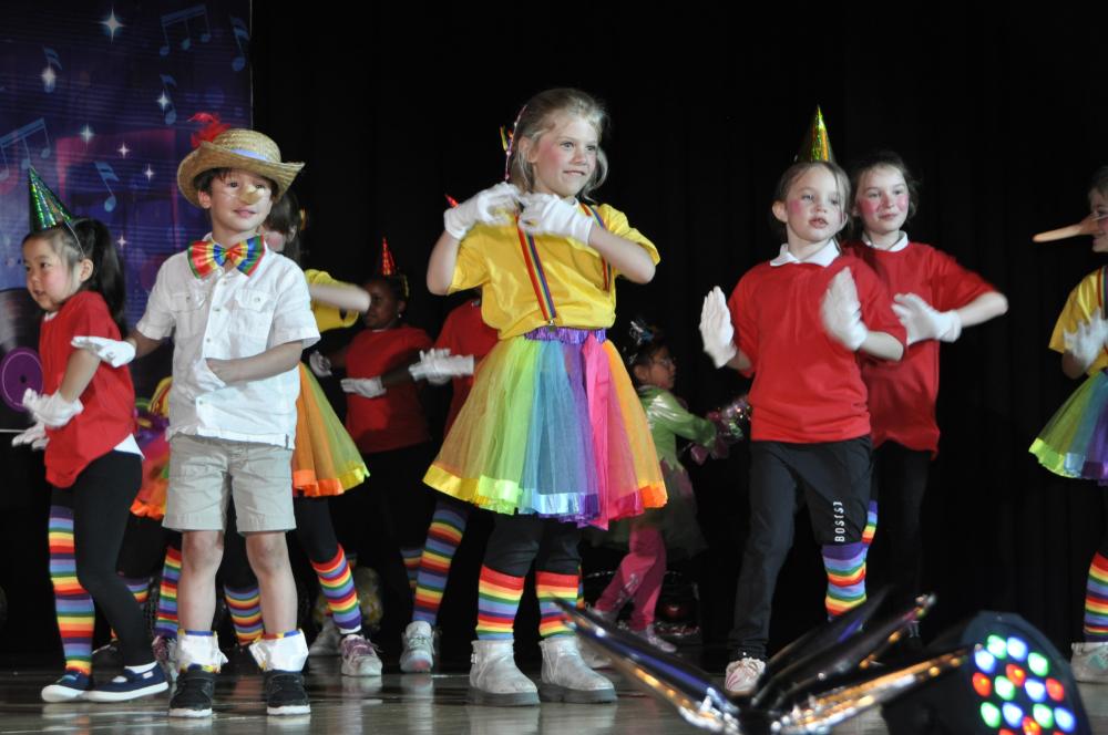 Kids dressed like puppets in colorful clothing on stage smiling