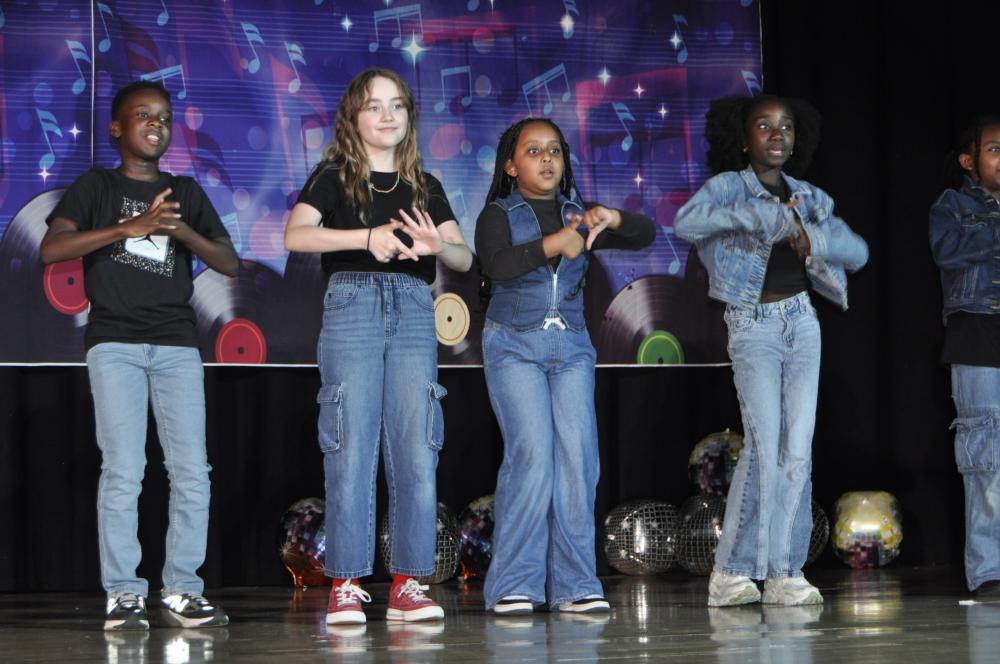 Kids dressed in black tops and jeans on stage dancing