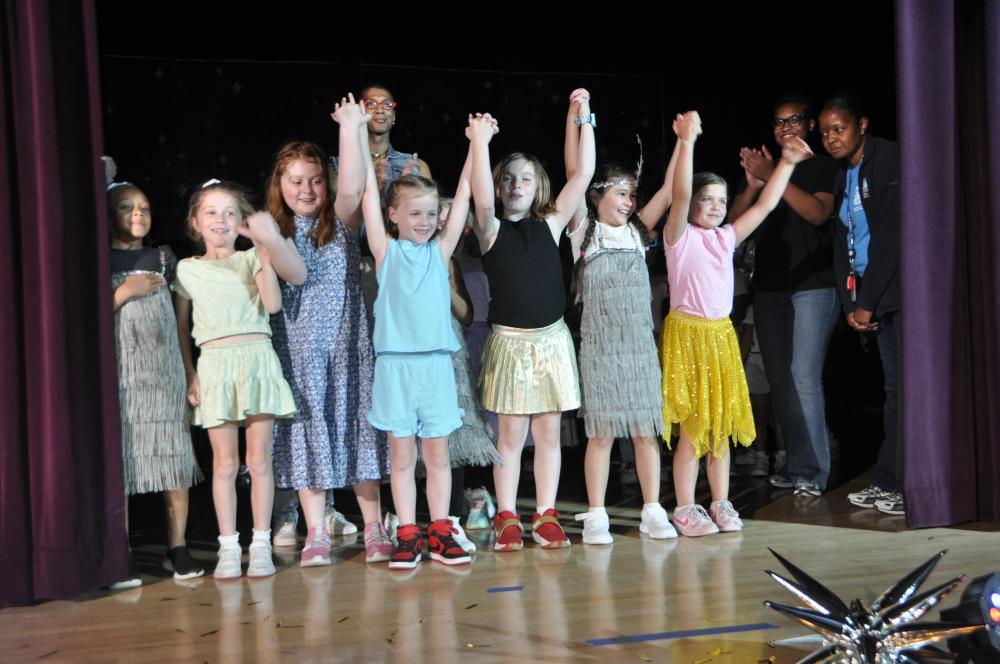 Kids holding hands with their arms up on stage getting ready to bow before the crowd