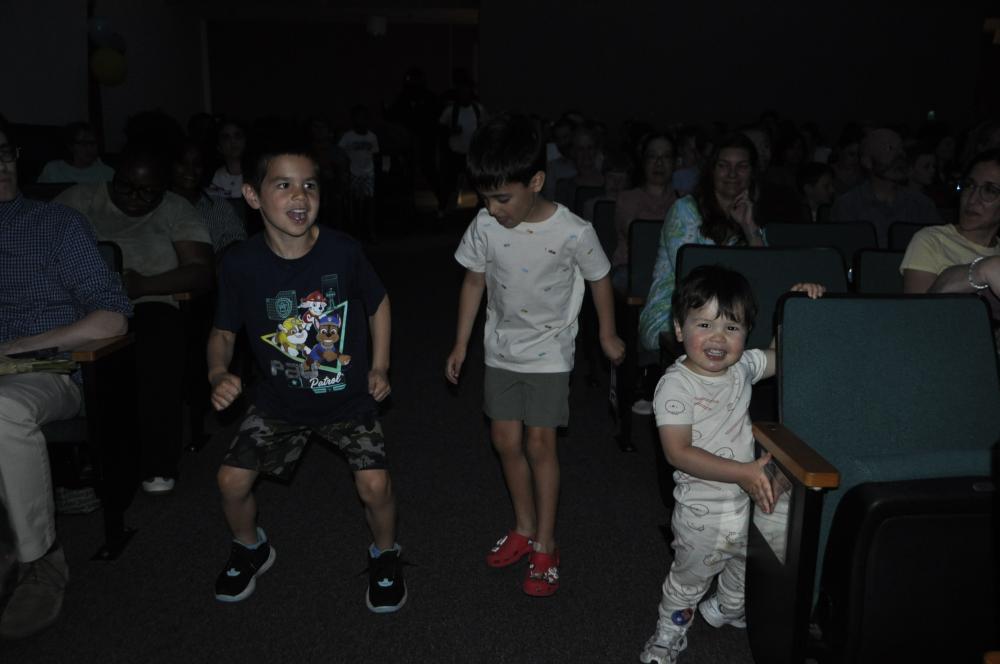 Three young boys dancing and smiling in between the auditorium seats at the Lee Center
