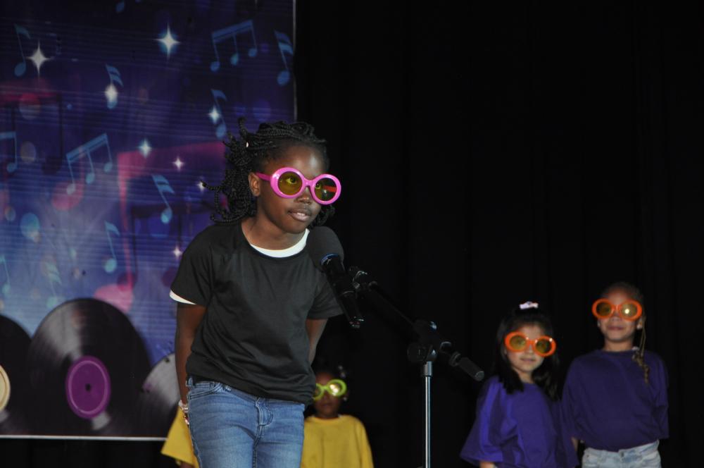 Young girl dressed in a black shirt and jeans with big, pink rimmed glasses