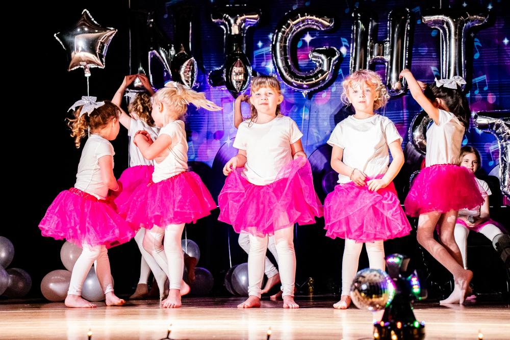 Performers wearing white shirts and pink tutus on stage