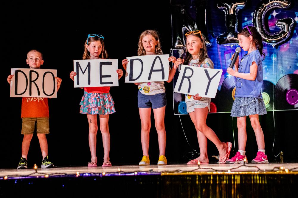 Performers holding posters with the letters DRO on the first poster, then ME, then DA, then RY on the last poster